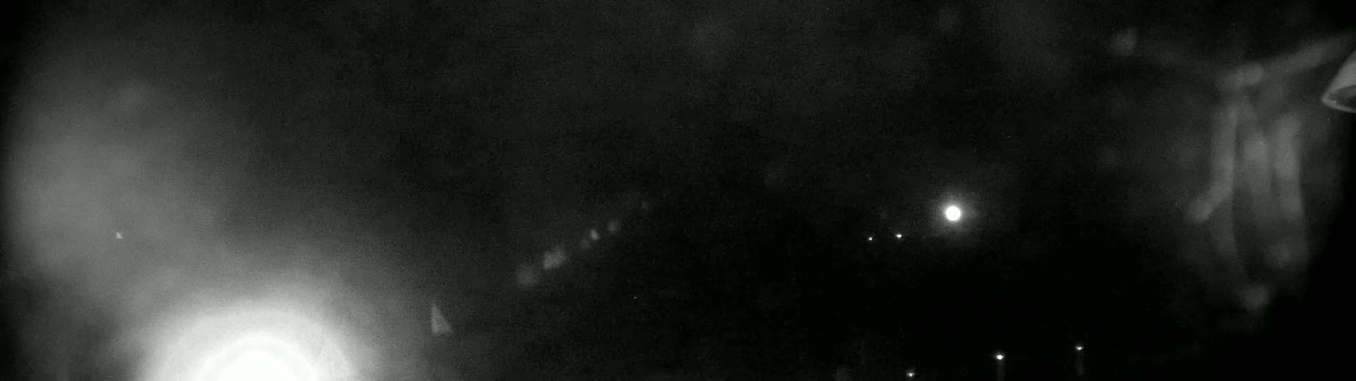 A nighttime scene shows blurry lights in the distance, and a bright light, possibly a streetlight or moon, closer to the viewer in hazy or foggy conditions.