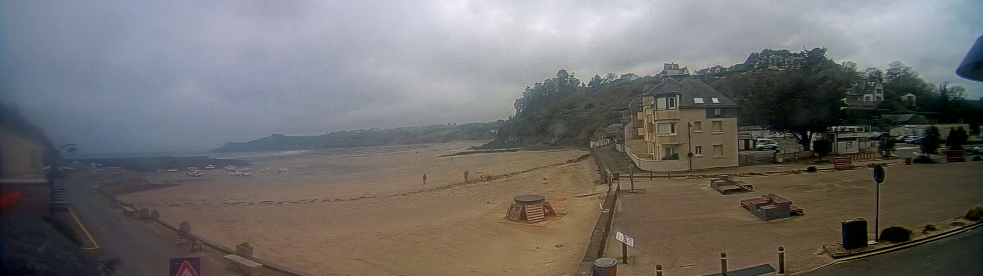 A sandy beach stretches out under an overcast sky, with a multi-story building and a few cars visible near the shore.
