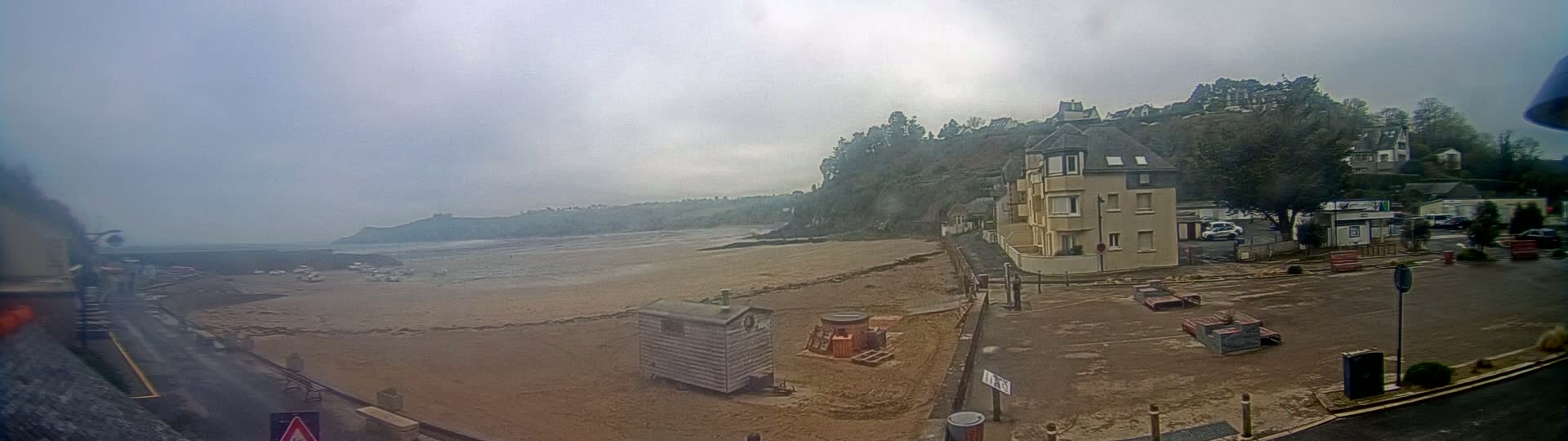 A sandy beach is visible at low tide, near a seaside town with buildings on a hillside under an overcast sky.