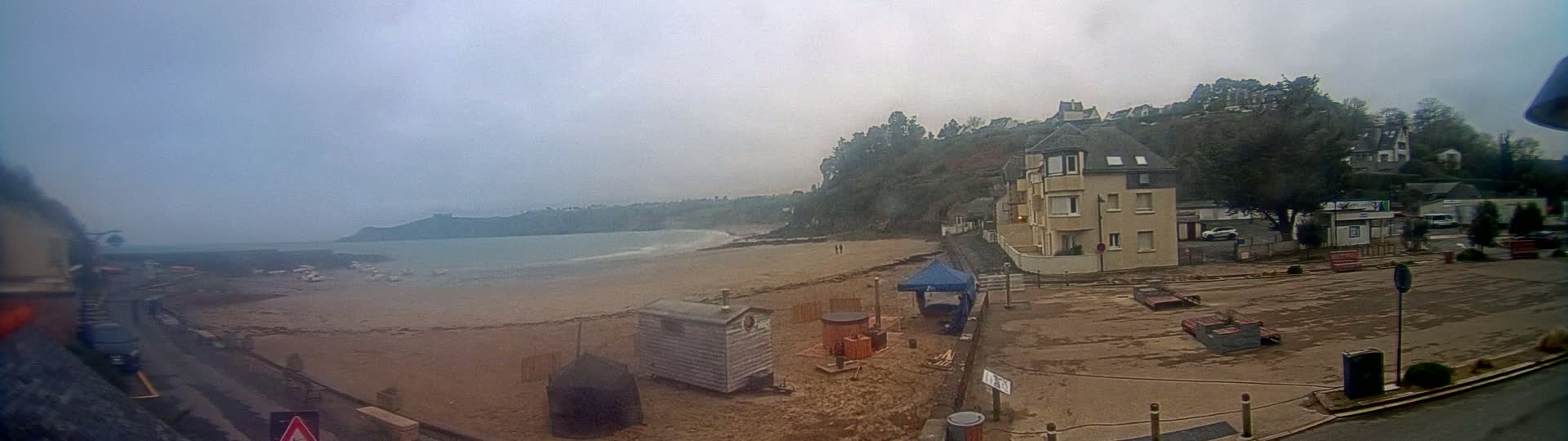 A sandy beach with a few boats and buildings is visible under an overcast sky, with a light-colored building in the center.