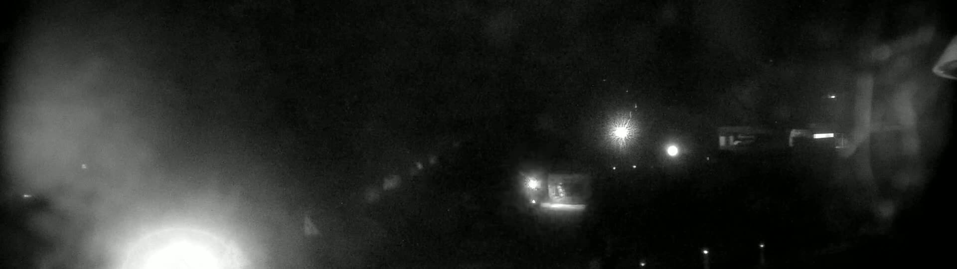 A blurry, nighttime image shows a few indistinct lights in the distance, possibly from buildings or vehicles, under a dark, possibly snowy or hazy sky.