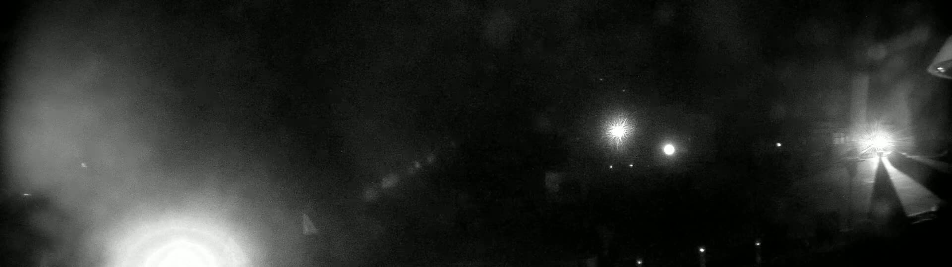 A nighttime scene shows a blurry collection of bright lights and shadows in foggy conditions.