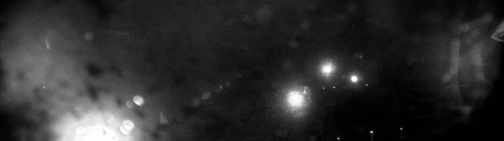 A blurry, nighttime image shows several bright lights in the distance through a rain-streaked window.