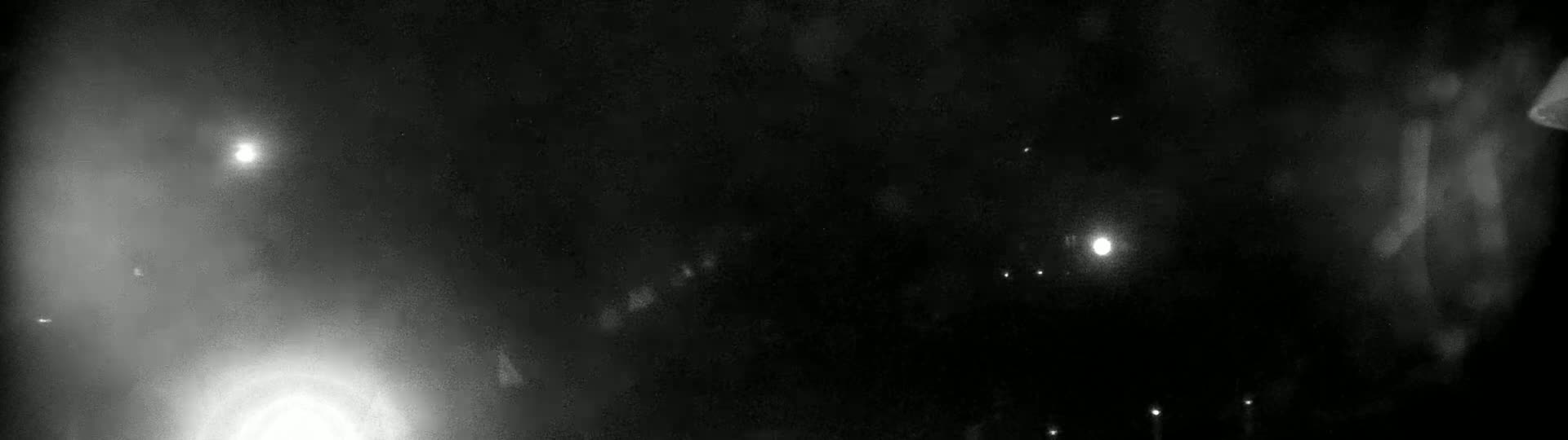 A hazy, dark nighttime scene shows several bright lights in the distance, possibly streetlights or stars.