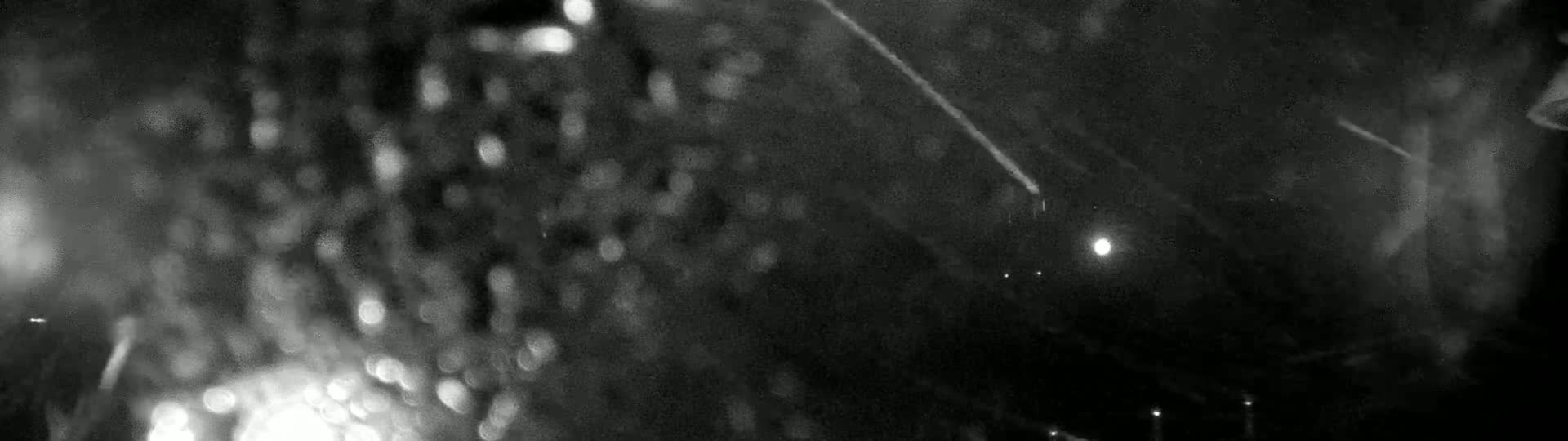 A blurry, out-of-focus nighttime scene shows streaks of rain or snow against a dark background with bright lights.
