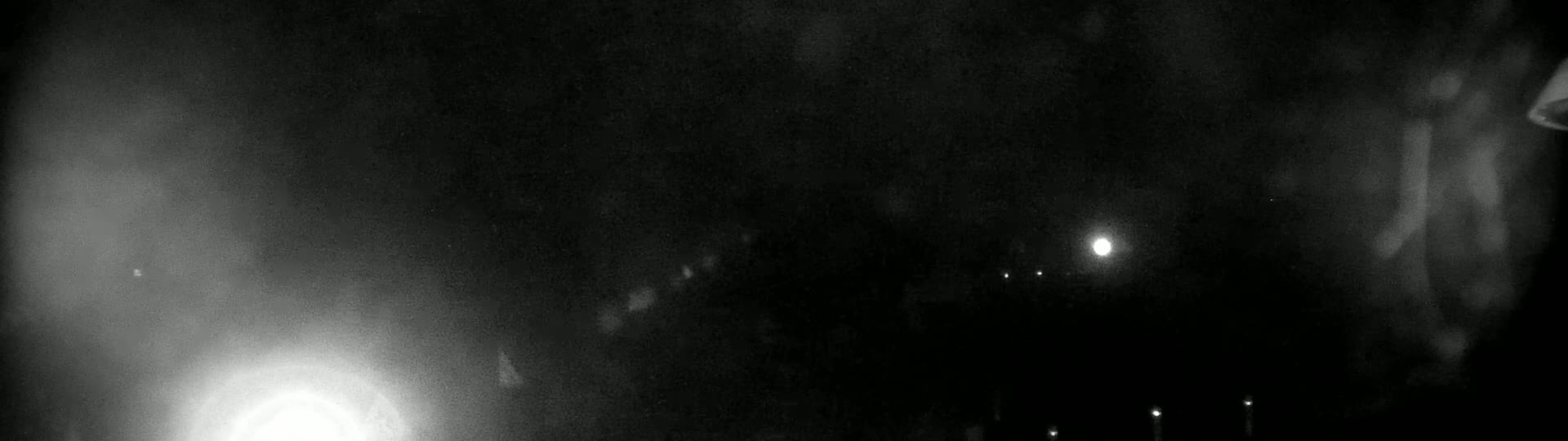 A nighttime, blurry image shows a bright light source to the lower left, several fainter lights in the distance, and hazy, indistinct shapes in the foreground and background.