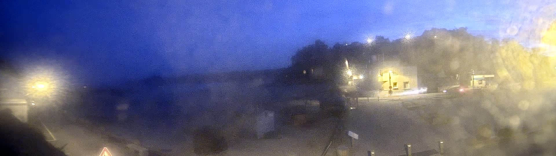 A blurry nighttime view of a street scene with a building, vehicles, and streetlights, obscured by what appears to be rain or snow.