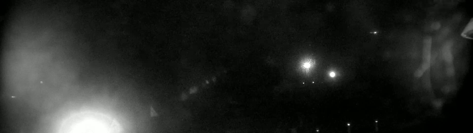 A dark, nighttime scene shows several bright lights, possibly from distant vehicles or streetlights, against a hazy, dark sky.
