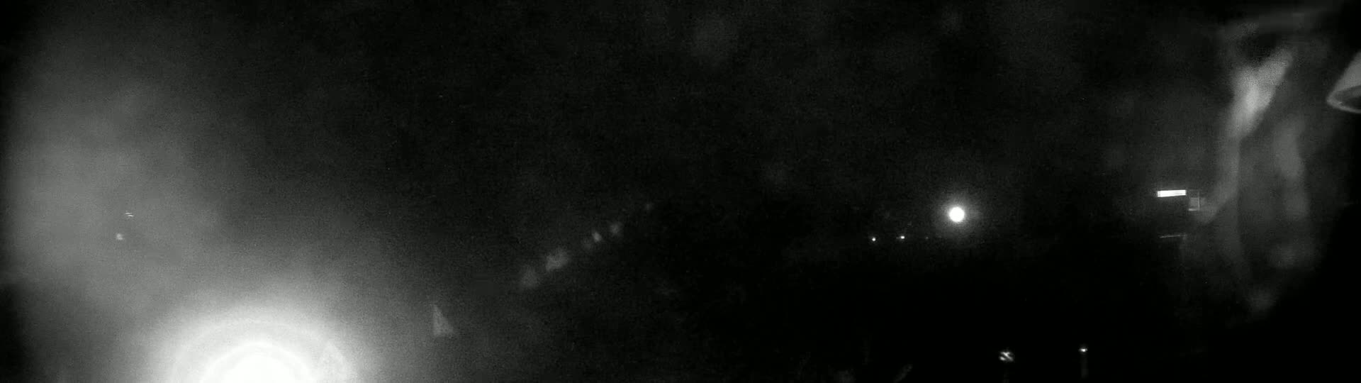 A blurry, dark, nighttime scene shows a bright light in the lower left and several fainter lights scattered throughout.