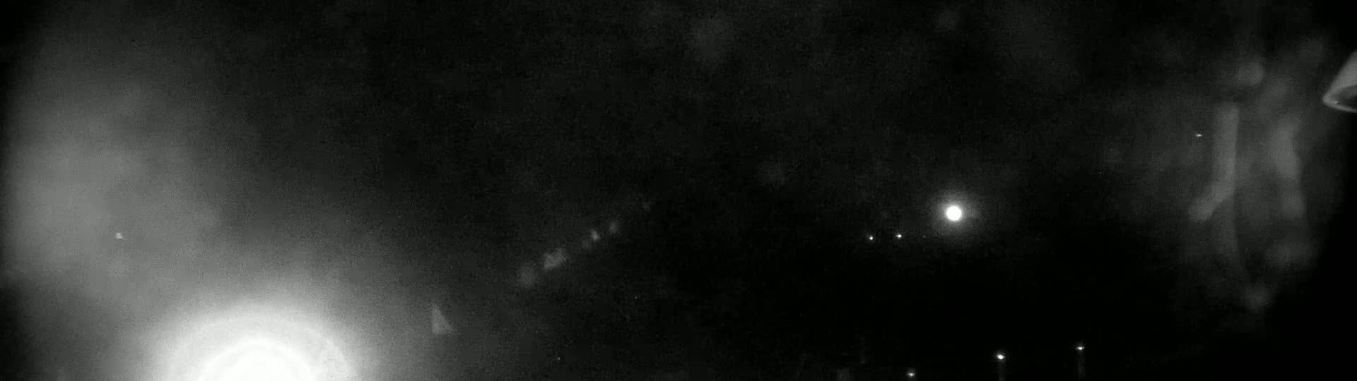 A grainy, dark image shows a bright light in the lower left corner and several fainter lights at the bottom and in the center, against a mostly black background.