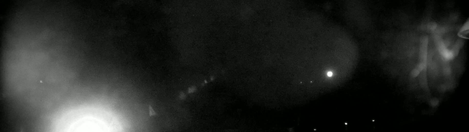 A blurry, dark nighttime image shows a bright light in the lower left corner and several smaller, fainter lights scattered across the mostly black scene.