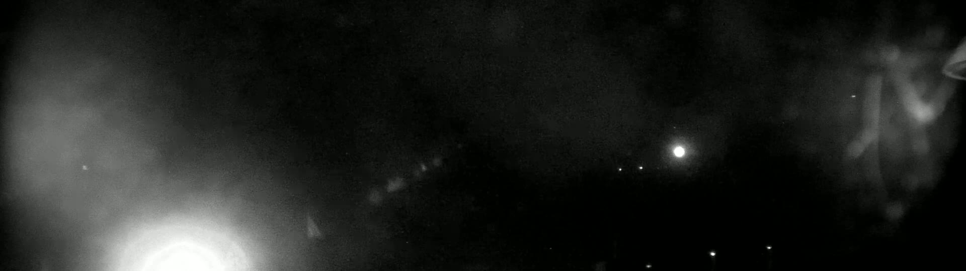 A blurry, nighttime image shows several bright lights, possibly from distant sources, in a dark, hazy sky.