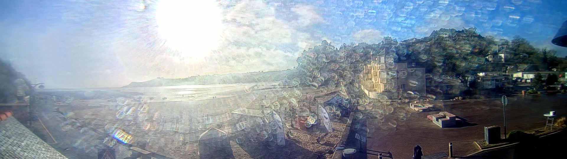 A sunny, hazy day at a beach with buildings and people visible through a rain-covered window.