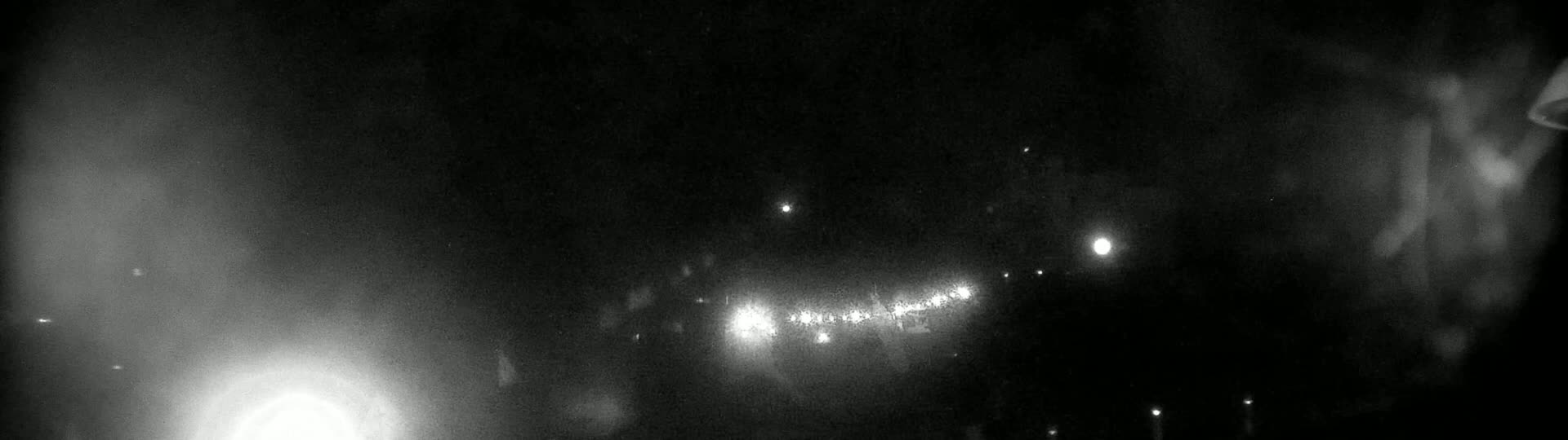 A hazy, dark night scene shows a line of lights in the distance, possibly a roadway, with brighter lights interspersed among them.