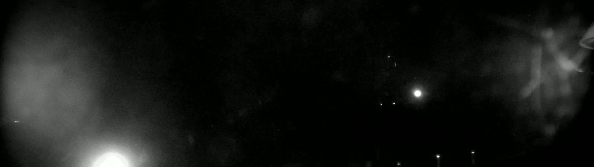 A blurry, grainy nighttime image shows several faint lights in the distance, possibly stars or streetlights, against a dark, hazy sky.