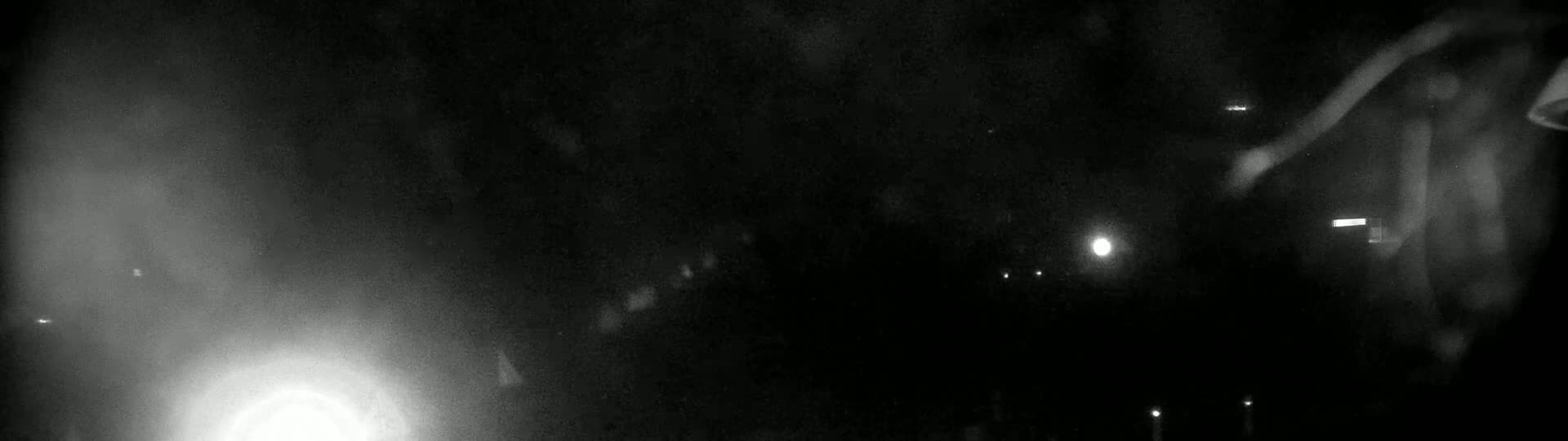 A blurry, low-light nighttime image shows indistinct shapes and a few bright lights in the distance.