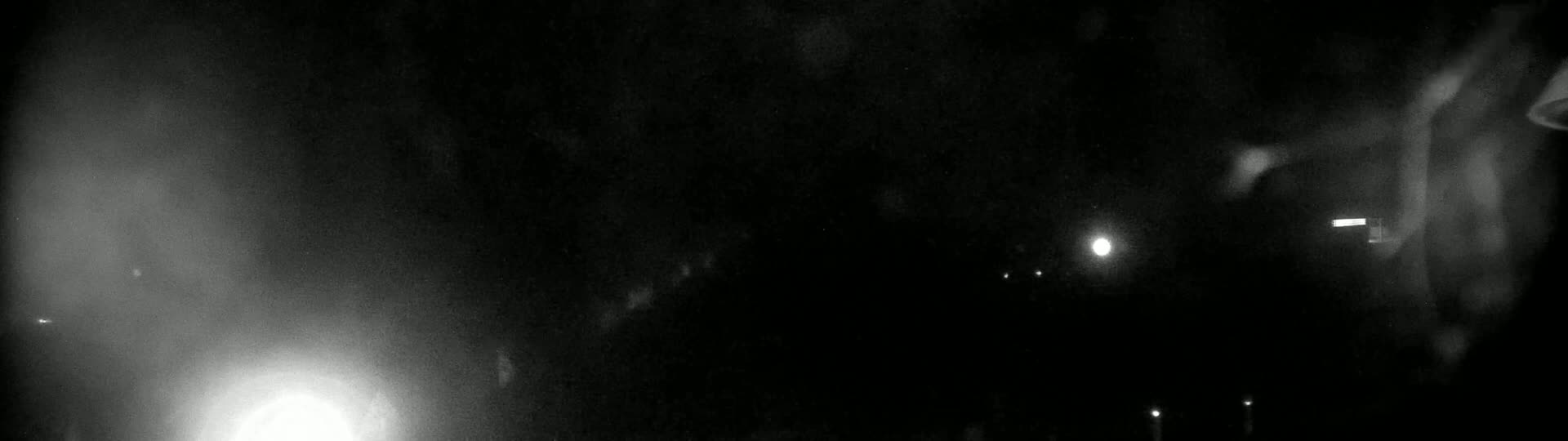 A nighttime, blurry, low-light image shows a dark scene with a few faint lights visible in the distance, possibly streetlights.