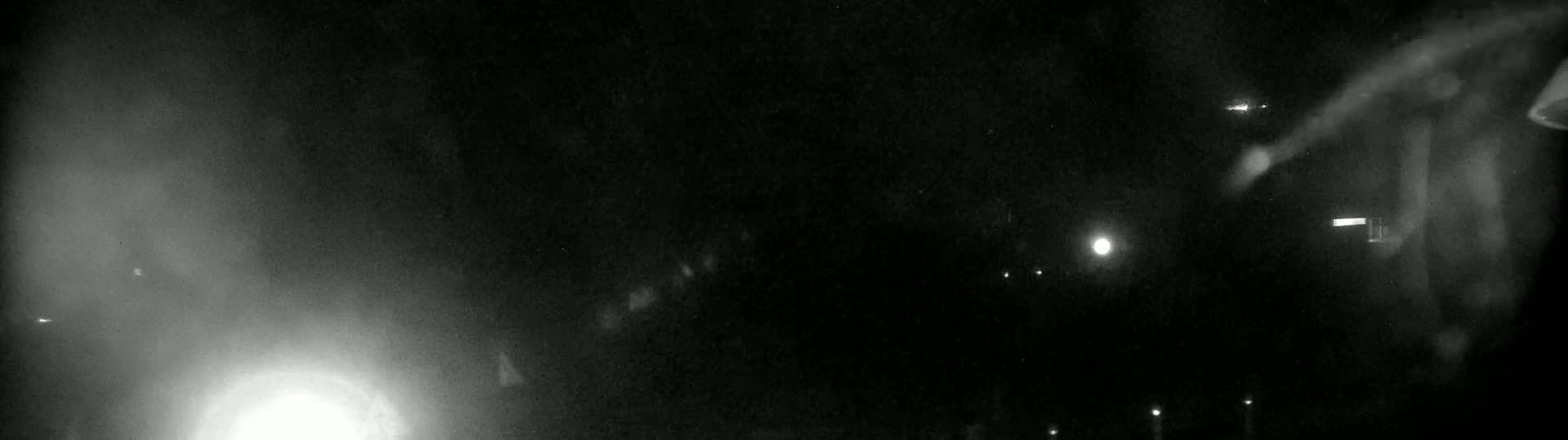A grainy, nighttime image shows indistinct shapes and bright lights in the distance, possibly from vehicles or streetlights.