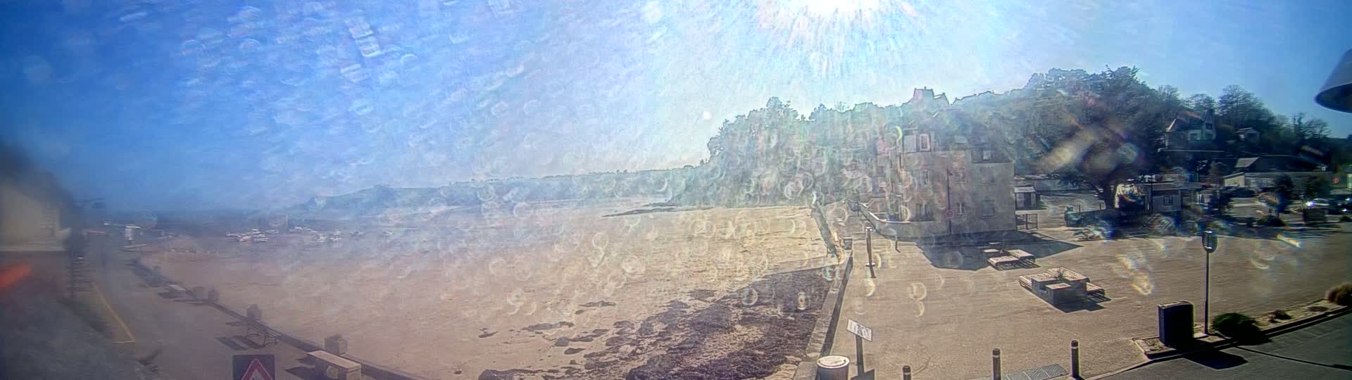 A sunny day reveals a sandy beach, a calm body of water, and buildings situated on a hill overlooking the shore.