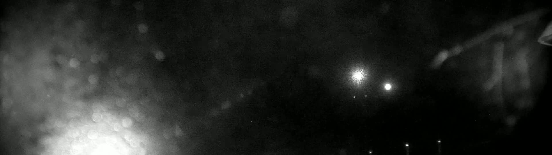 A nighttime, blurry view of several bright lights, possibly streetlights, through a rain-streaked window or windshield.