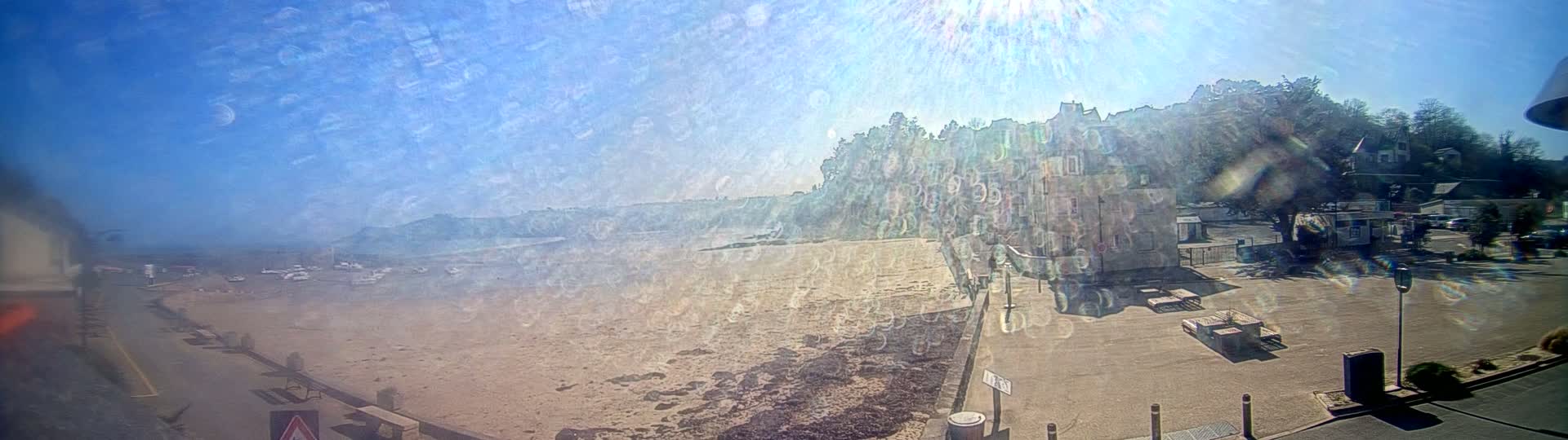 A sandy beach with a few boats in the water is visible below buildings on a sunny day.