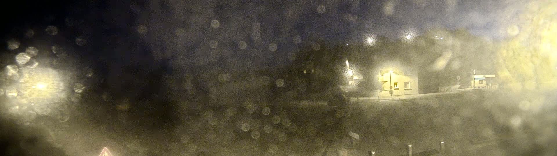 A blurry nighttime view of a building and streetlights, seen through a rain-covered window.