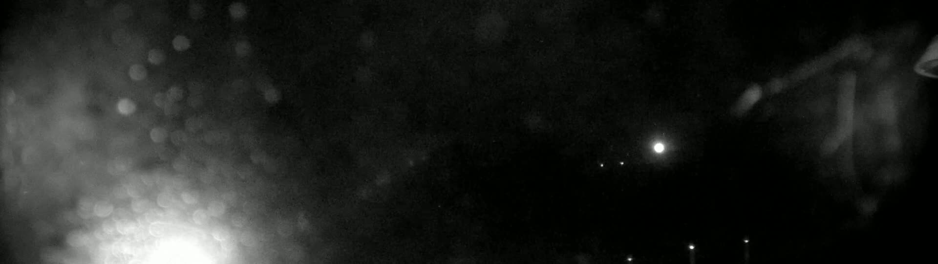 A nighttime, blurry outdoor scene shows bright lights and what appears to be rain or snow.