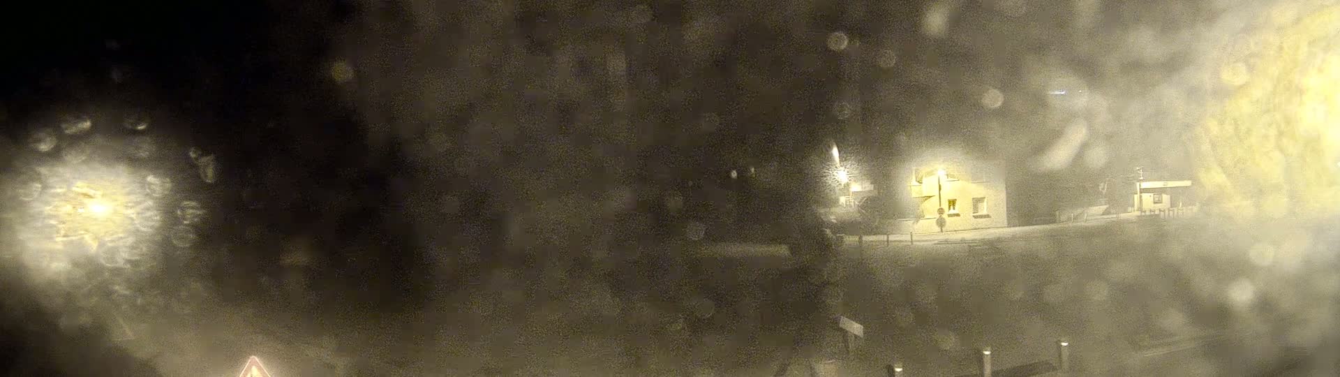 A blurry nighttime view of a building illuminated by a streetlight in snowy conditions.