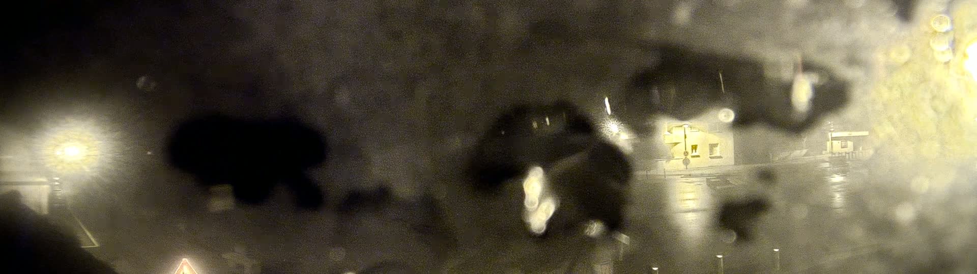 A blurry nighttime scene viewed through a rain-covered window shows indistinct buildings and lights.