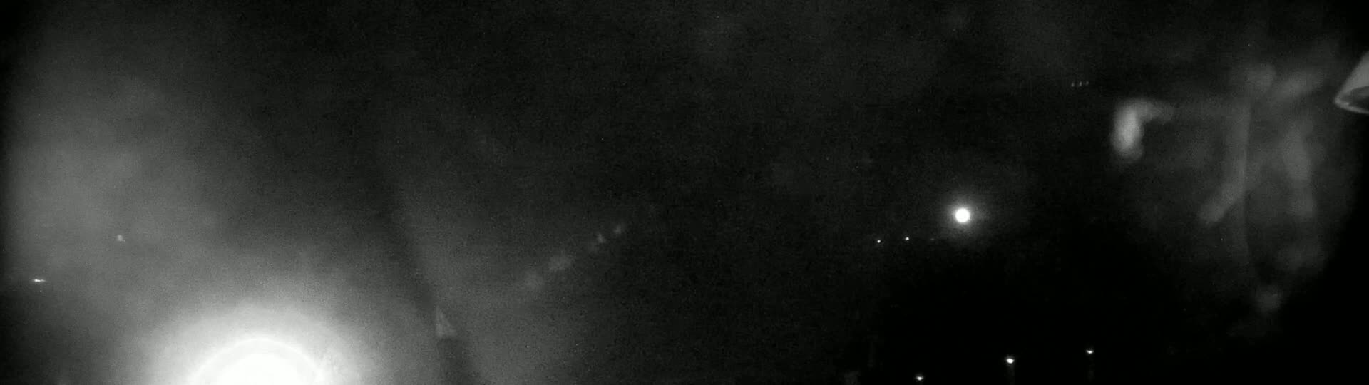A blurry, nighttime image shows a dark, possibly hazy or foggy scene with a few faint lights in the distance.