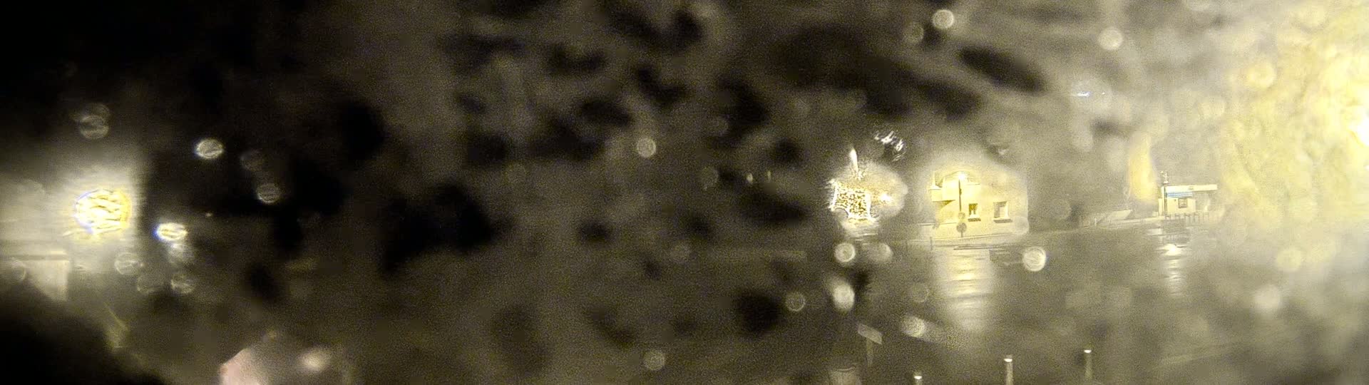 A blurry, nighttime view of a building and streetlights seen through a rain-covered window.