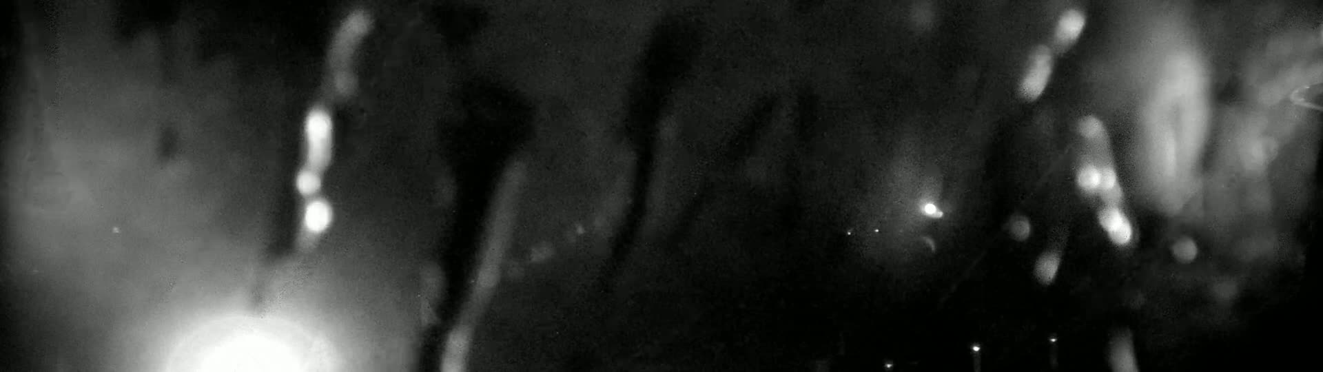 Blurry, out-of-focus shapes and bright lights are visible through a wet or foggy surface at night.
