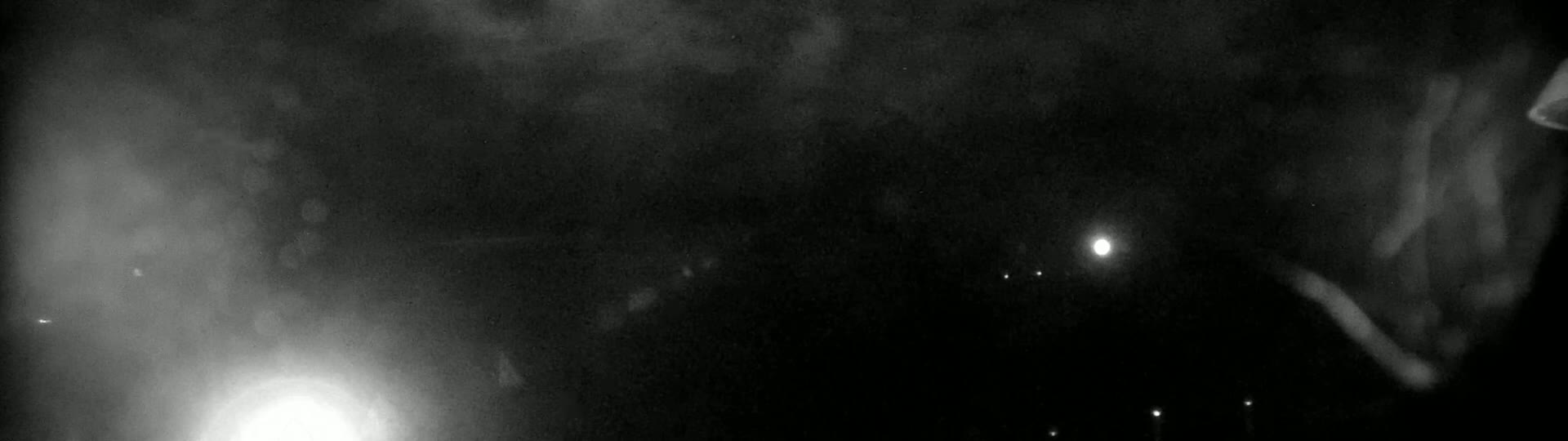 A nighttime, hazy or foggy scene shows several distant lights and bright light sources in the darkness.
