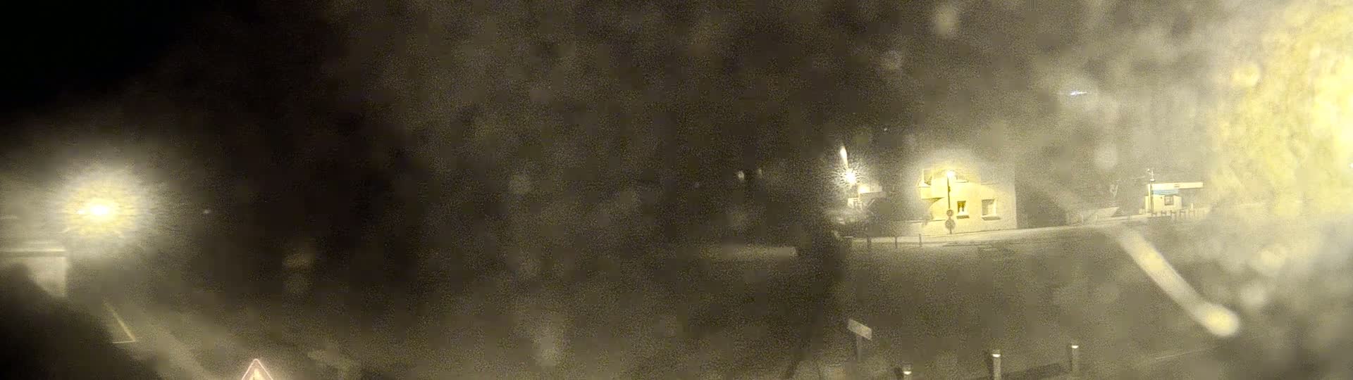 A blurry nighttime scene shows a building lit by a streetlight in snowy or dusty conditions.