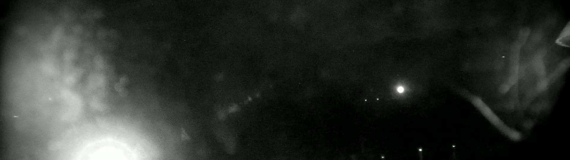 A hazy, dark nighttime scene shows a bright light in the distance, with several dimmer lights visible further away.