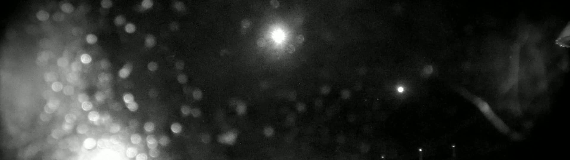 A nighttime, blurry scene shows out-of-focus lights and what appears to be rain or snow falling.