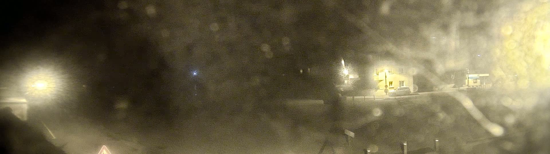 A blurry nighttime scene shows a building and a car through a rain-covered window.