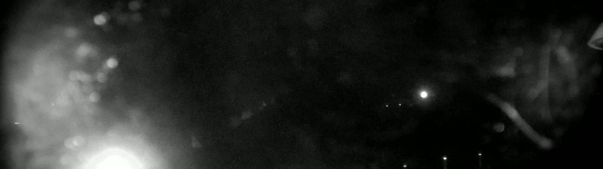 A blurry, nighttime image shows indistinct shapes and bright lights in the dark, possibly caused by rain or snow.