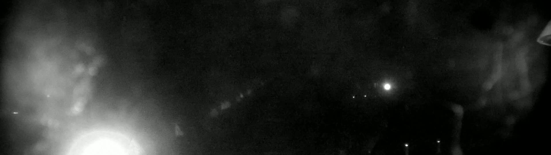 A hazy, dark nighttime scene shows blurry lights in the distance and a bright light source in the lower left corner.
