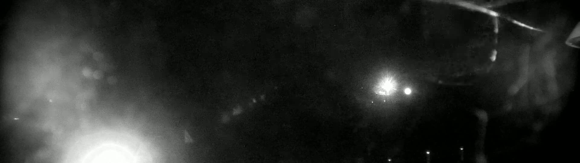 A dark, blurry night scene shows bright lights in the distance and hazy atmospheric conditions.