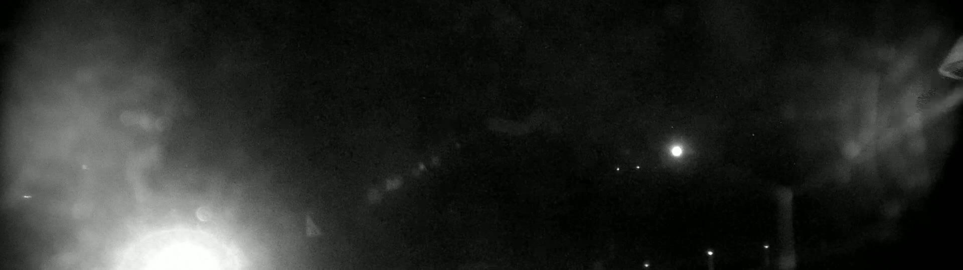 A nighttime scene shows hazy bright lights and a few dim lights in the distance under a dark, possibly foggy or cloudy sky.
