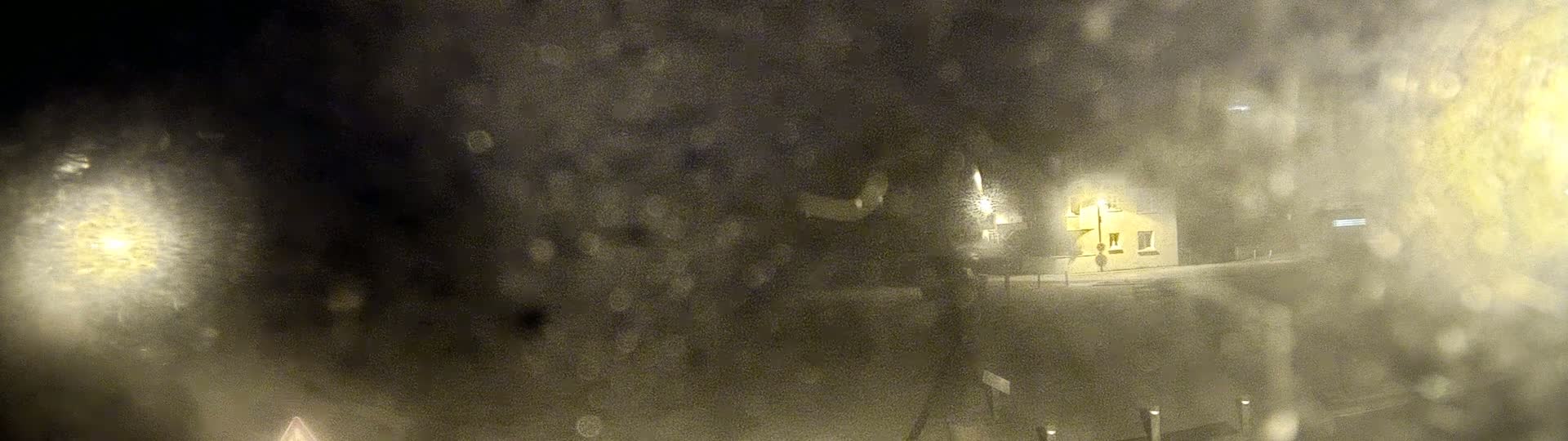 A blurry nighttime view through a rain-covered window shows a dimly lit building and street.