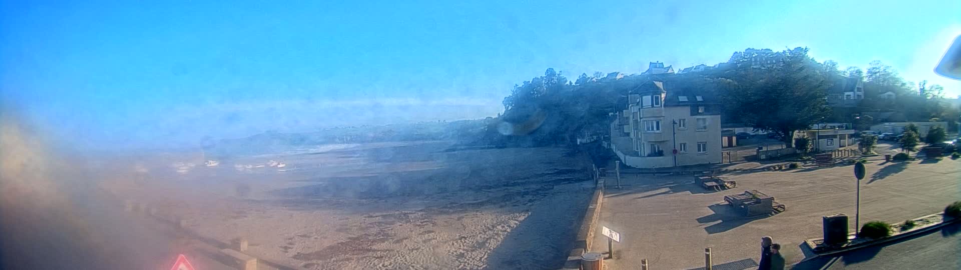 A hazy, sunny day reveals a sandy beach, calm ocean waves, and a seaside town with buildings perched on a hillside.
