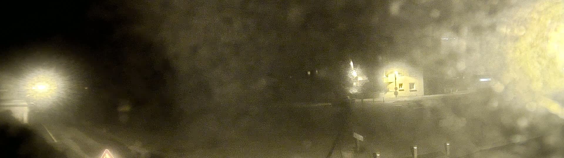 A blurry nighttime scene of a road and building obscured by heavy snow or fog.