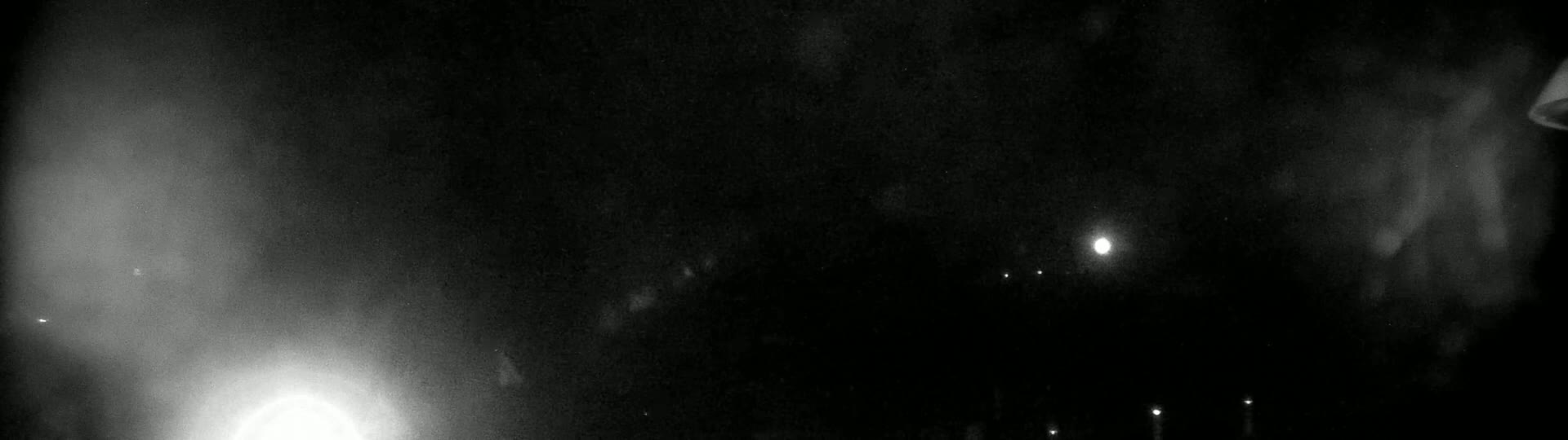 A nighttime, hazy, outdoor scene shows a bright light in the center, with several dimmer lights below it and a brighter area to the left.