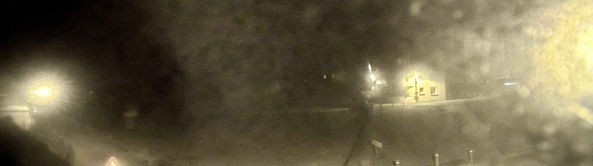 A blurry nighttime image shows a building illuminated by a streetlight in snowy conditions.