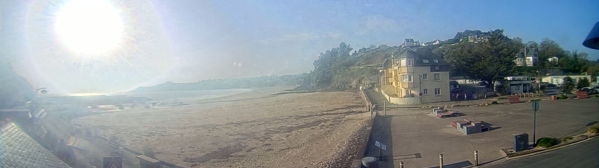 A sandy beach stretches below a hillside town on a bright, sunny day.