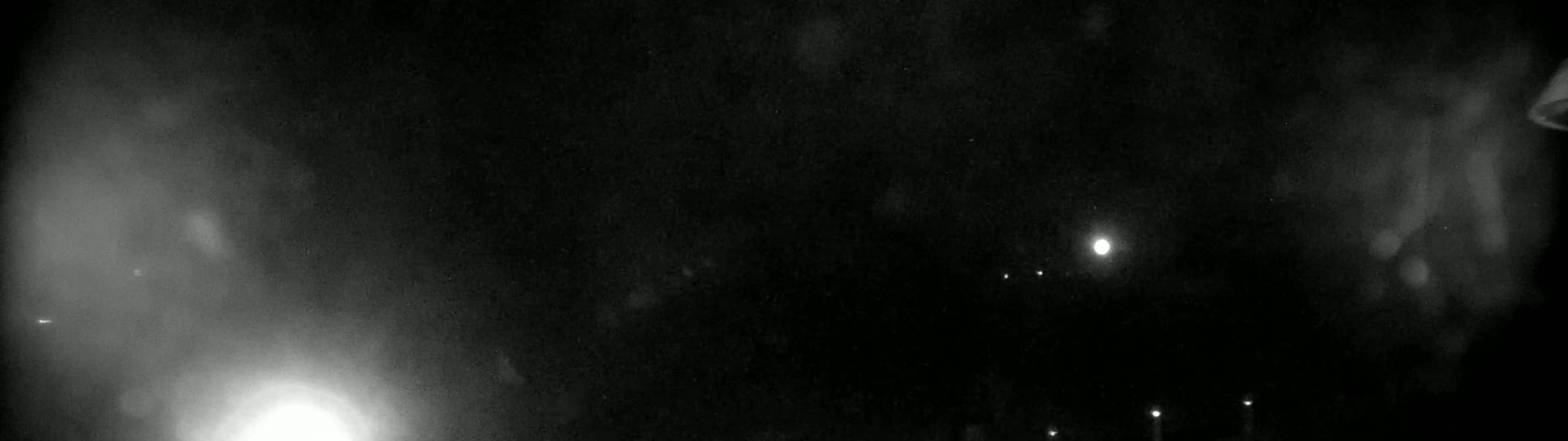 A nighttime outdoor scene shows a hazy, dark sky with a bright light source and several fainter lights in the distance.