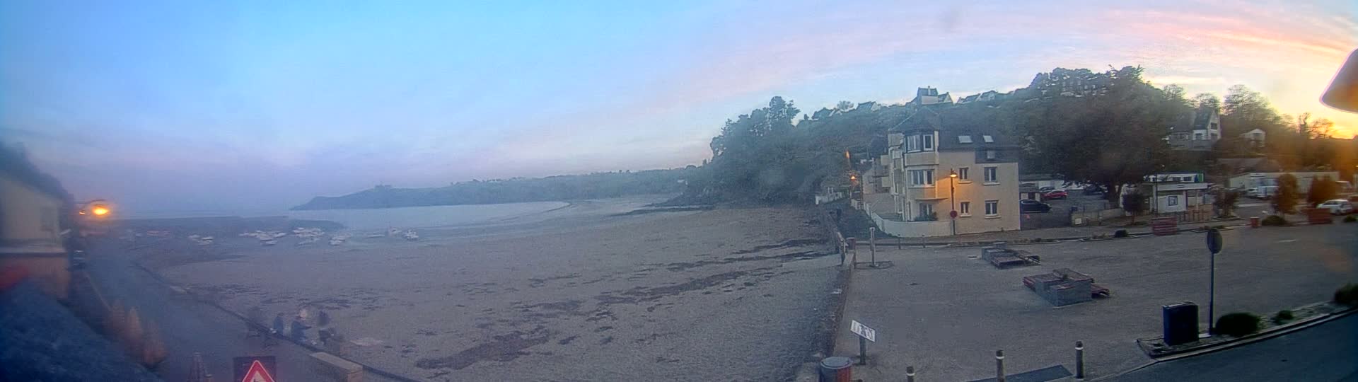 A sandy beach with several boats at low tide is visible, next to a residential area at dawn under a mostly clear sky.