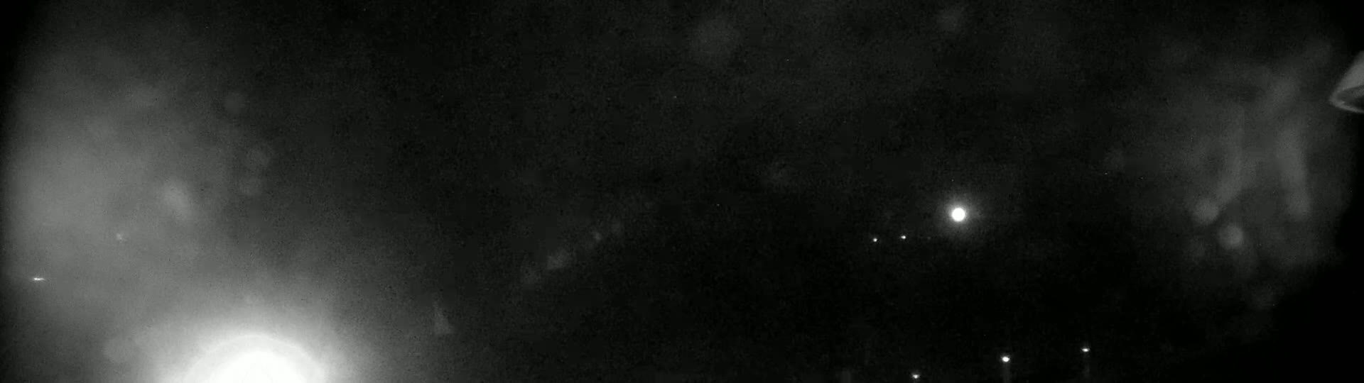 A nighttime outdoor scene shows a hazy, dark sky with several small, distant lights and a brighter light in the lower portion of the image.